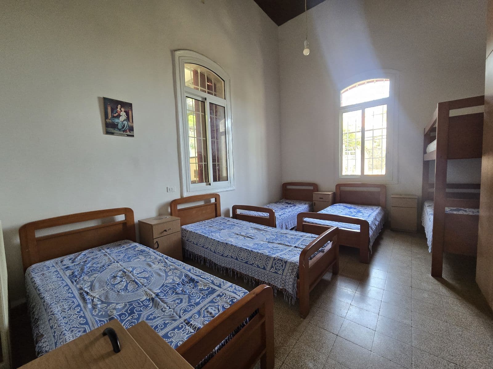 A bedroom at the Home with three beds under blue bedspreads and an arched window.