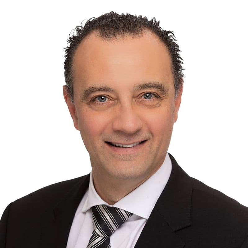 Portrait de Bassam Tochan, souriant, en costume et cravate.