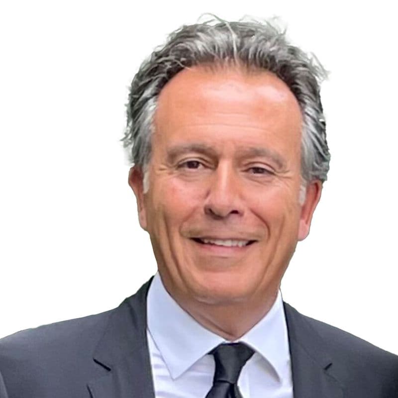 Portrait de Fadi Melki, souriant, en costume, devant un mur de feuillage.